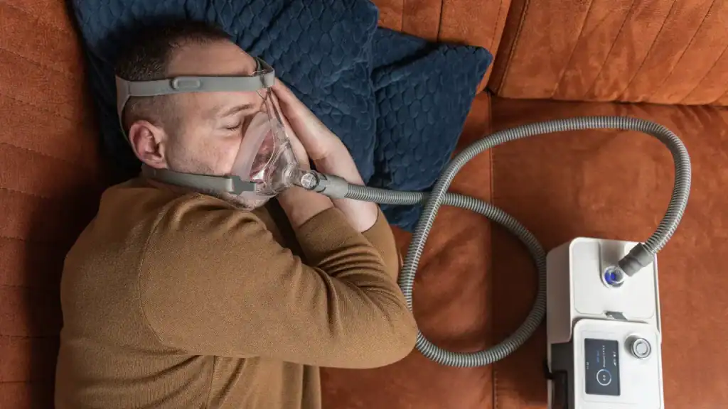 Man sleeping in bed on top of orange covers using a sleep apnea machine