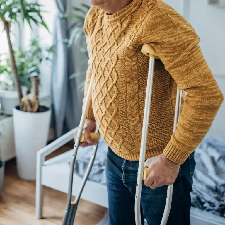 man in yellow sweater using crutches inside
