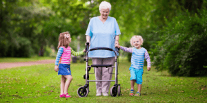 grandmother using a walker to walk on grass with her granddaughters,